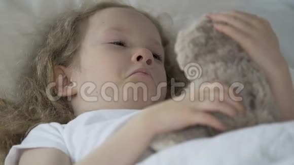 躺在床上抱着她的玩具熊在孤儿院哭着的小卷发孩子视频的预览图