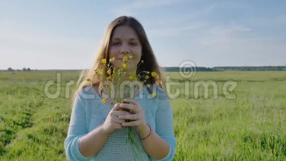 俄罗斯年轻女孩手里拿着一束花在温暖的夏天晚上在田野里摆姿势视频的预览图