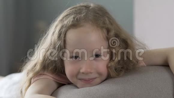 一个长着卷发的女孩躺在沙发上对着镜头微笑幸福视频的预览图