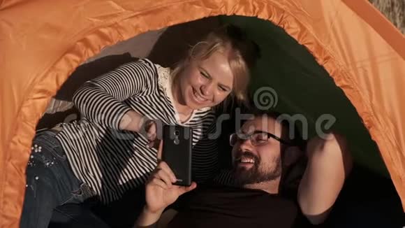 一对在帐篷里的幸福夫妇正在看电话里的东西笑着视频的预览图