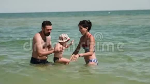 快乐的父母和孩子在海里玩耍父亲在旋转手里拿着儿子母亲在努力视频的预览图