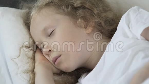 美丽的卷发金发孩子睡在床上健康的睡眠特写视频的预览图