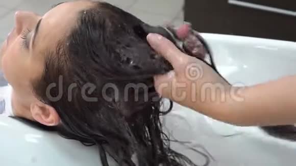 美容师发型师在美容院里照顾一个黑发女孩的头发按摩头发擦油膏视频的预览图