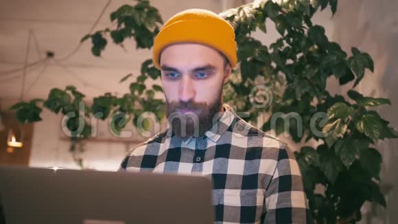 戴着黄色帽子的嬉皮士使用笔记本电脑坐在咖啡馆或同事间工作视频的预览图