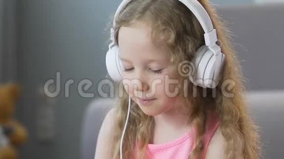 漂亮的卷发女孩用耳机听音乐和唱歌视频的预览图