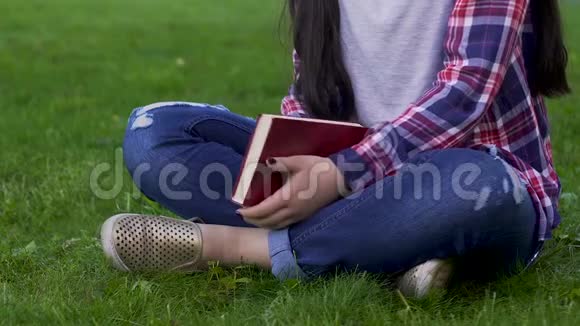 年轻女子坐在草地上拿着合上的书娱乐活动放松视频的预览图