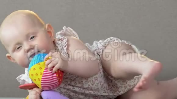 可爱的女婴躺在沙发上试图咬橡胶玩具托儿所视频的预览图