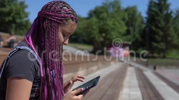 一个女孩坐在公园的长椅上使用平板电脑视频的预览图
