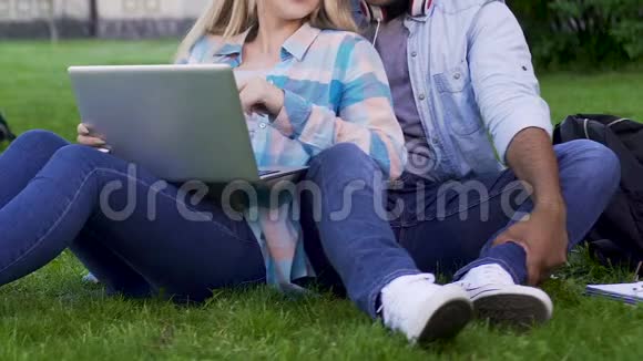 两个年轻人坐在草地上女孩靠在盖伊身上拿着笔记本电脑视频的预览图