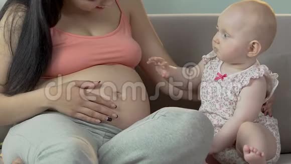 小女孩和孕妇坐在沙发上孩子轻轻地打着肚子视频的预览图