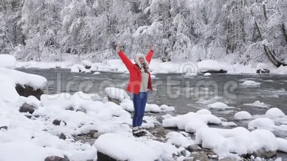 在一条山河的河岸上的女人享受着寒冷的冬天的早晨呼吸着寒冷的空气快乐着视频的预览图