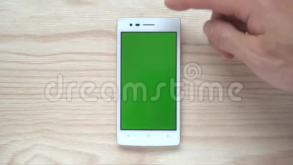 木制背景下的人滑动智能手机或手机绿色屏幕视频的预览图