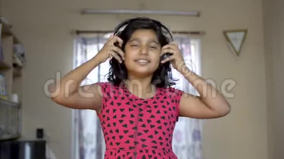 可爱的印度亚裔白种人女孩喜欢在手机上听音乐耳机点头和跳舞的肖像正面观看视频的预览图