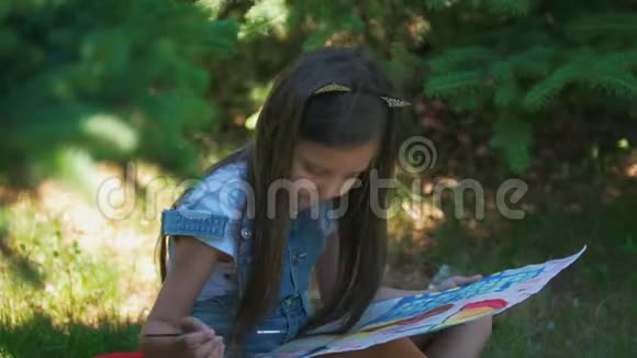 可爱的女孩画着明亮的图画在夏天的公园里水粉坐在草地上视频的预览图