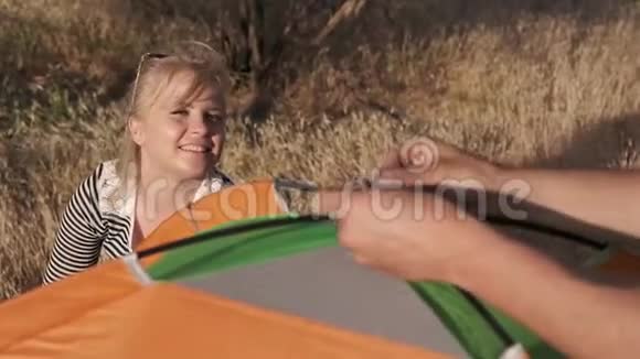 一个年轻的女人在微笑和交谈而一个年轻的男人在搭帐篷视频的预览图