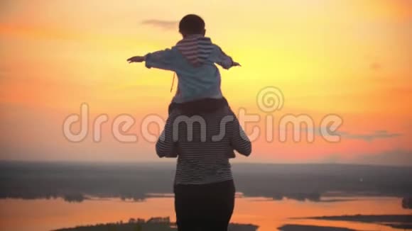 母亲和她的小儿子在鲜红的夕阳下玩得很开心母亲把孩子抱在肩上孩子挥动双手视频的预览图