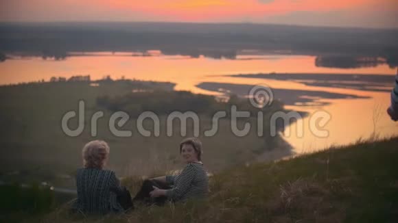 祖母和母亲在夏天的傍晚看着夕阳坐在草地上孩子们走向他们视频的预览图