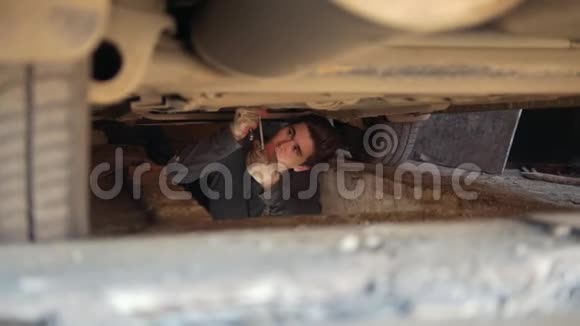 年轻的男性机械师在汽车下面从托盘下拧开部件视频的预览图