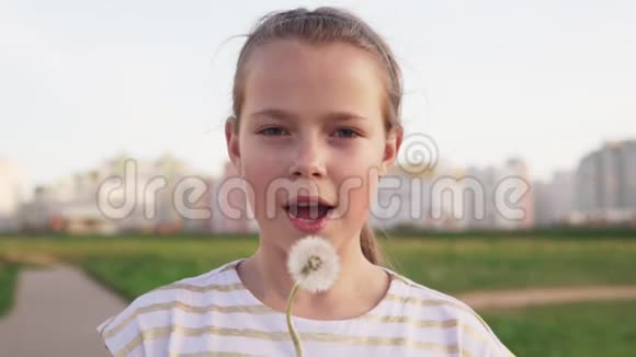 可爱的小女孩吹着蒲公英在城市草坪上微笑视频的预览图
