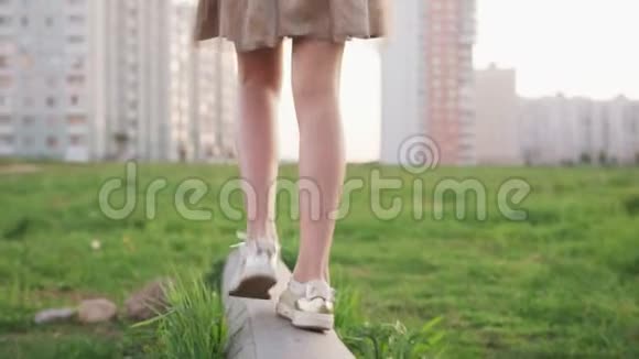 小女孩的腿在水泥原木上行走在城市草坪上的草地上跳跃视频的预览图