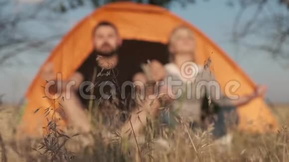 一对背景的夫妇正在帐篷前冥想呼吸平静并在前面的地面上释放出来视频的预览图