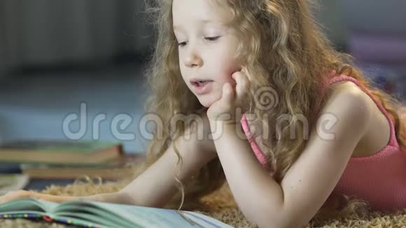 可爱的卷发女孩躺在地毯上大声朗读童话故事快乐的童年视频的预览图