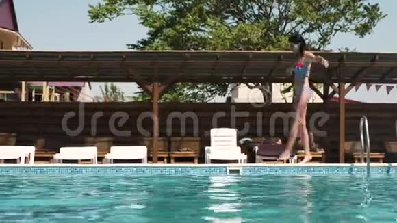 一位身穿泳衣的年轻女子兴高采烈地沿着游泳池的边缘散步视频的预览图