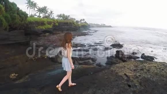 日落时分女孩沿着美丽海岸的岩石漫步巴厘岛慢动作视频的预览图