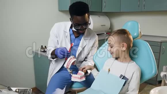 在牙医办公室里一个小的男性病人和非洲年轻的牙医一起学习牙科护理视频的预览图