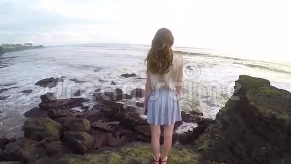 美丽而高大的女孩站在巴厘岛海洋海岸的岩石上视频的预览图