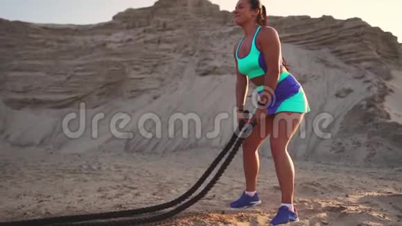 一个带绳子的女孩的特写在海滩附近的沙地上进行户外训练女人手中的绳索视频的预览图