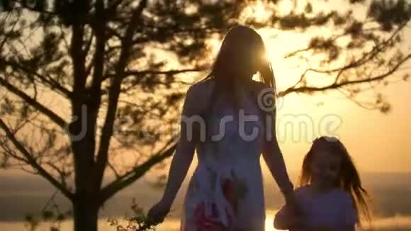 幸福的母女在灿烂的夕阳下走在树下的小山上视频的预览图