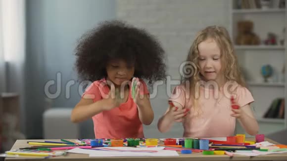 两个多种族的孩子坐在桌子旁用油漆弄脏了手视频的预览图