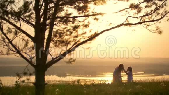 日落时分年轻女子在山上的一棵大树前为她的小女儿编织花圈视频的预览图