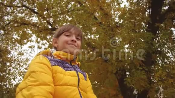 女孩把黄叶向上扔在秋天的公园里微笑慢动作视频的预览图