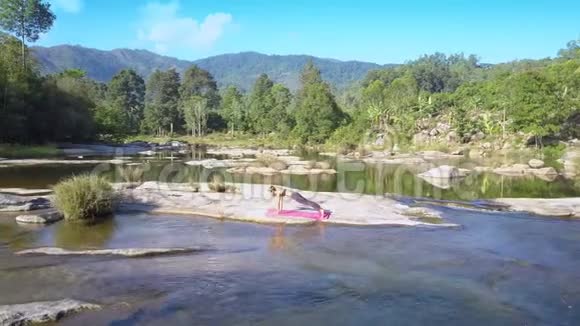 女孩用瑜伽对抗平静的河流在岩石中流淌视频的预览图