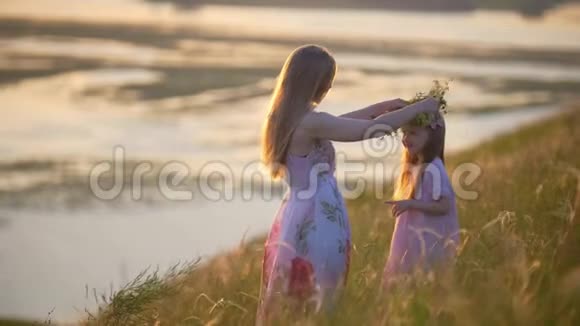 夏天日落时分可爱的母亲把花环戴在女儿的头上视频的预览图