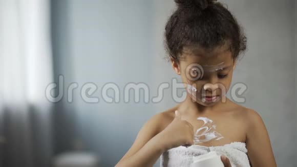 小女孩在身体和脸上涂上保湿霜模仿母亲的行为视频的预览图