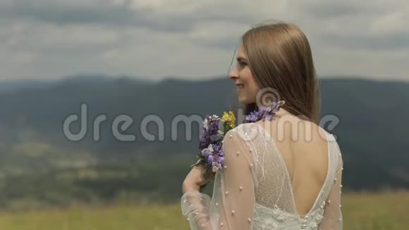 美丽的新娘穿着婚纱留在山上带着鲜花视频的预览图