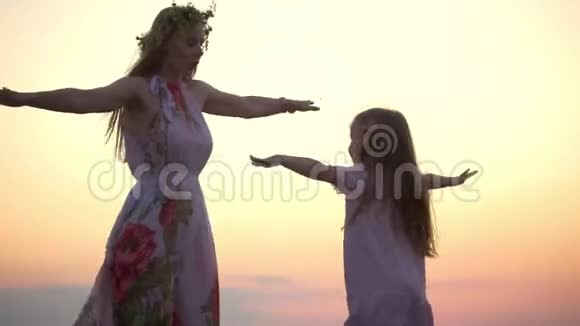 白种人女人头上戴着花环小女儿穿着夏装日落时分在山上跳舞视频的预览图