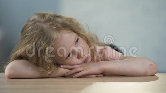 沮丧的卷发女孩子坐在桌子旁梦想着家庭视频的预览图