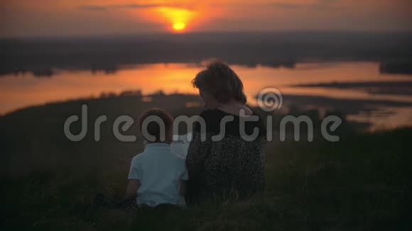 母亲和儿子坐在山上在夏天日落时看书视频的预览图