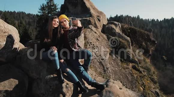 恋爱中的年轻夫妇坐在岩石上拍一张自拍参观著名旅游景点的男女视频的预览图