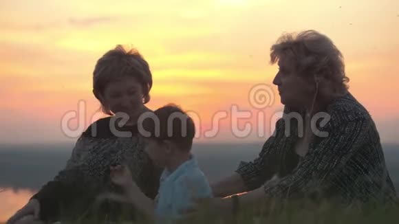 幸福的家庭祖母母亲和儿子坐在高高的山上在夏天的日落视频的预览图
