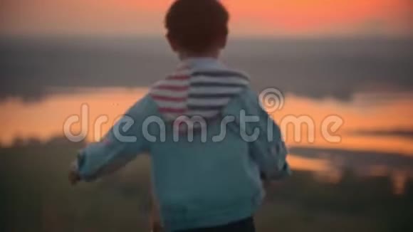 温暖的暑假年轻的妈妈坐在草地上看日落在河的背景下她的小儿子视频的预览图
