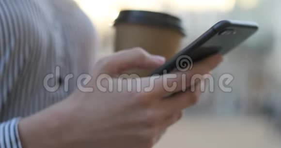一个女性拿着手机在户外滚动一个应用程序另一只手里拿着咖啡的特写镜头视频的预览图