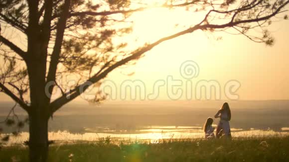日落时分年轻的母亲在山上的大树下为小女儿织了一个花环视频的预览图