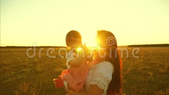 快乐的孩子拍手坐在一个笑妈妈的手上看着金色的太阳的日落慢动作视频的预览图