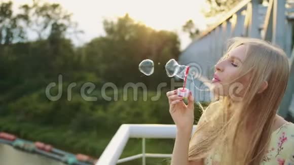 女人吹肥皂泡站在人行桥上的漂亮女人吹肥皂泡的侧视图视频的预览图