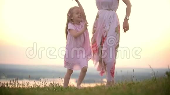 夏日的夕阳下快乐的小女孩牵着妈妈在草地上跳舞视频的预览图